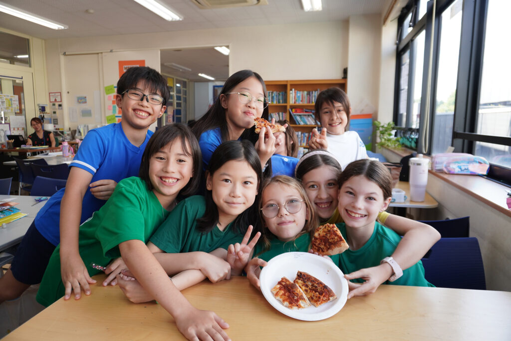 Lower School students at Tokyo International School smiling and eating pizza during pizza day.