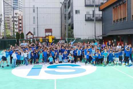 Wide shot of Tokyo International School students, faculty, and staff gathered on the outdoor track for a fundraising event, all wearing blue.